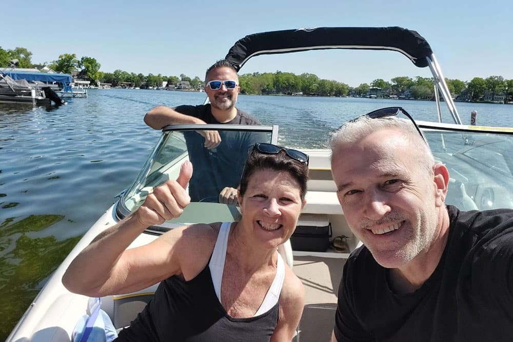 Three people taking a selfie on a boat with a scenic lake in the background.