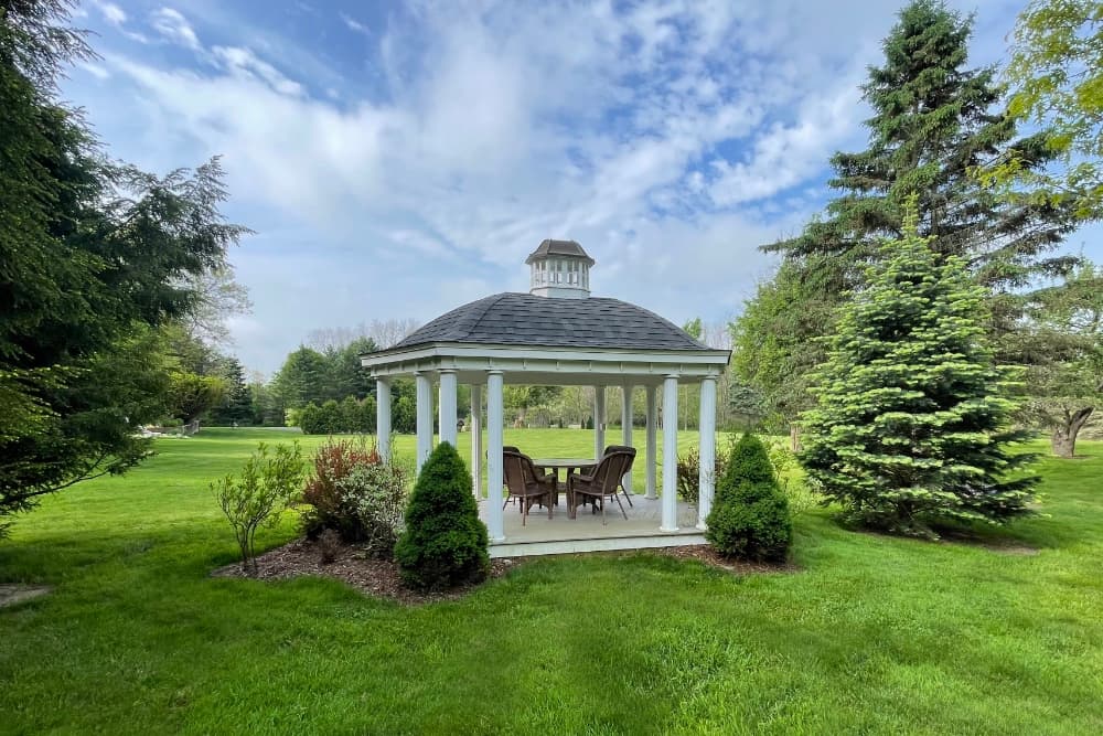 A white gazebo with a gray roof surrounded by lush green grass and trees.