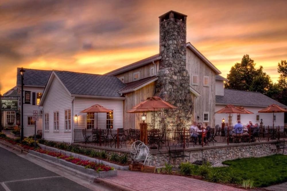 A charming restaurant with a stone chimney and outdoor seating under umbrellas, set against a vibrant sunset.