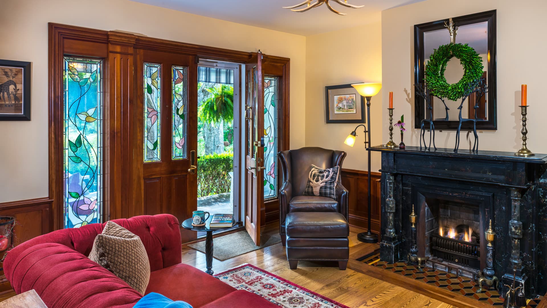 A cozy living room featuring a red sofa, a black fireplace, and large stained glass windows flanking the entry door.