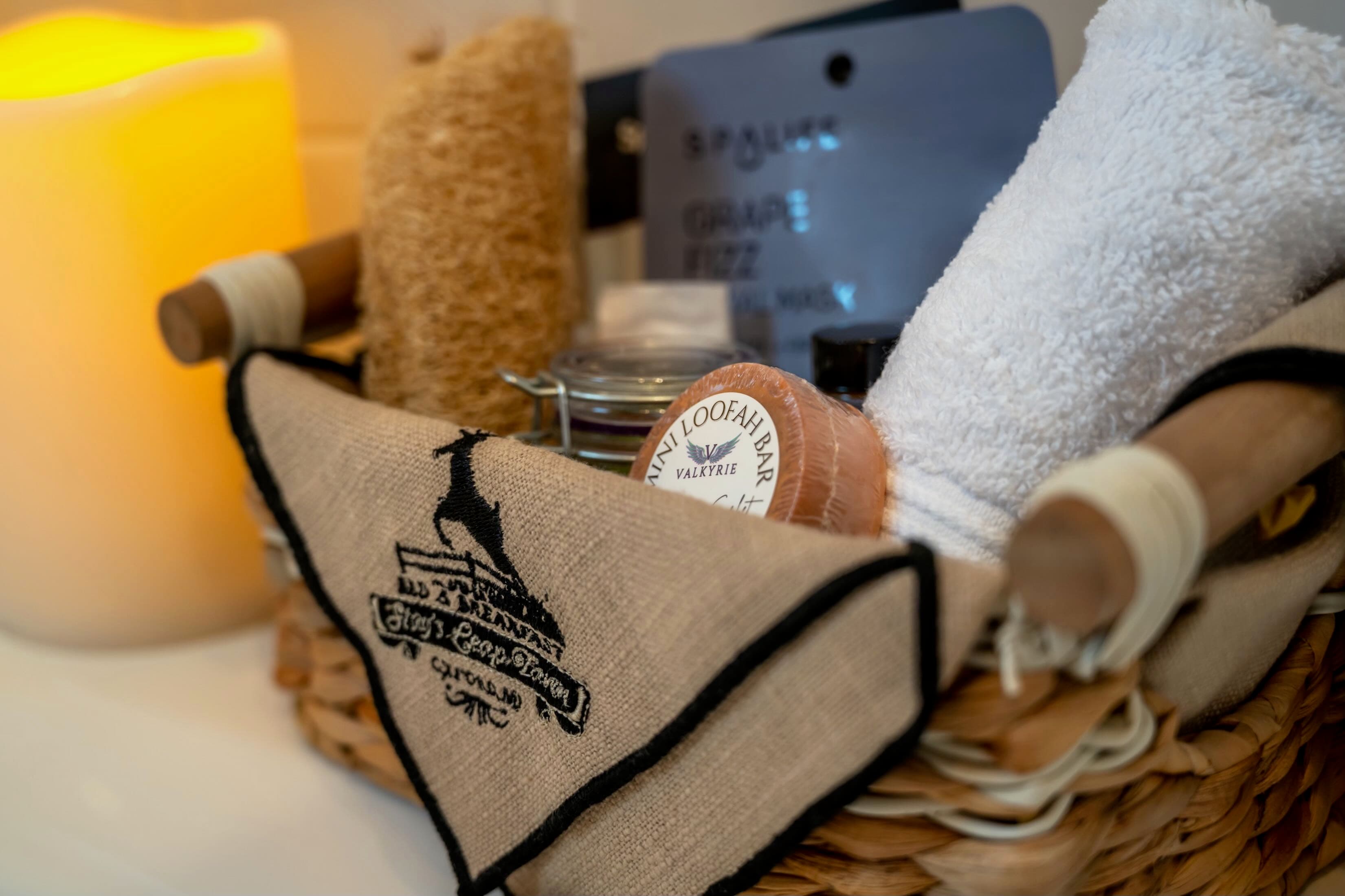A woven basket filled with bath essentials, including a loofah, towels, and a candle.