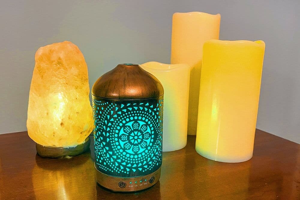 A decorative diffuser emits blue light, surrounded by glowing yellow candles and a salt lamp.