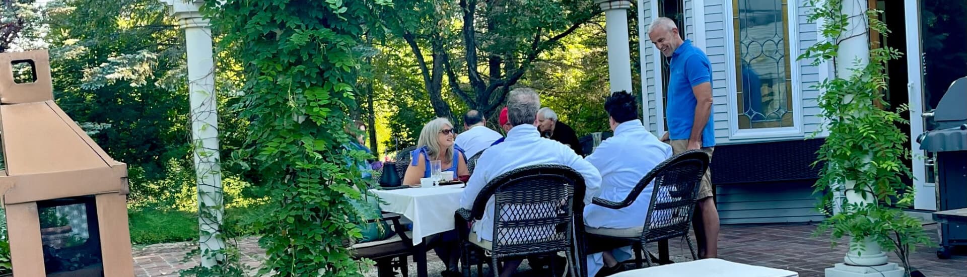 A group of people dining outdoors at a table surrounded by greenery.