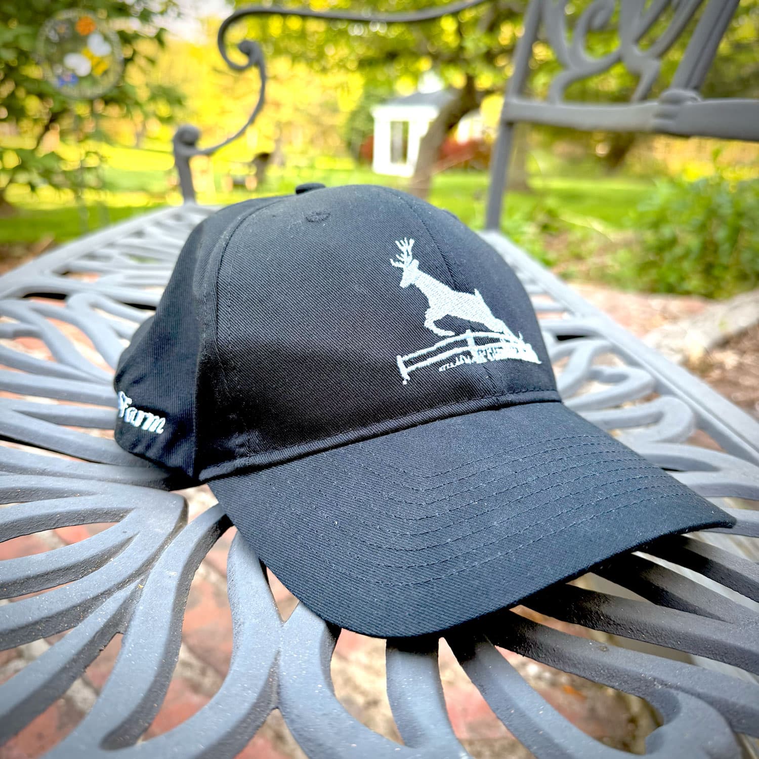 A black cap featuring a white embroidered deer design resting on a table outdoors.