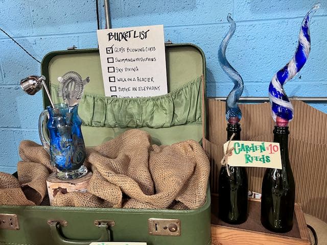 A vintage suitcase containing a bucket list, a glass piece, and decorative bottles.