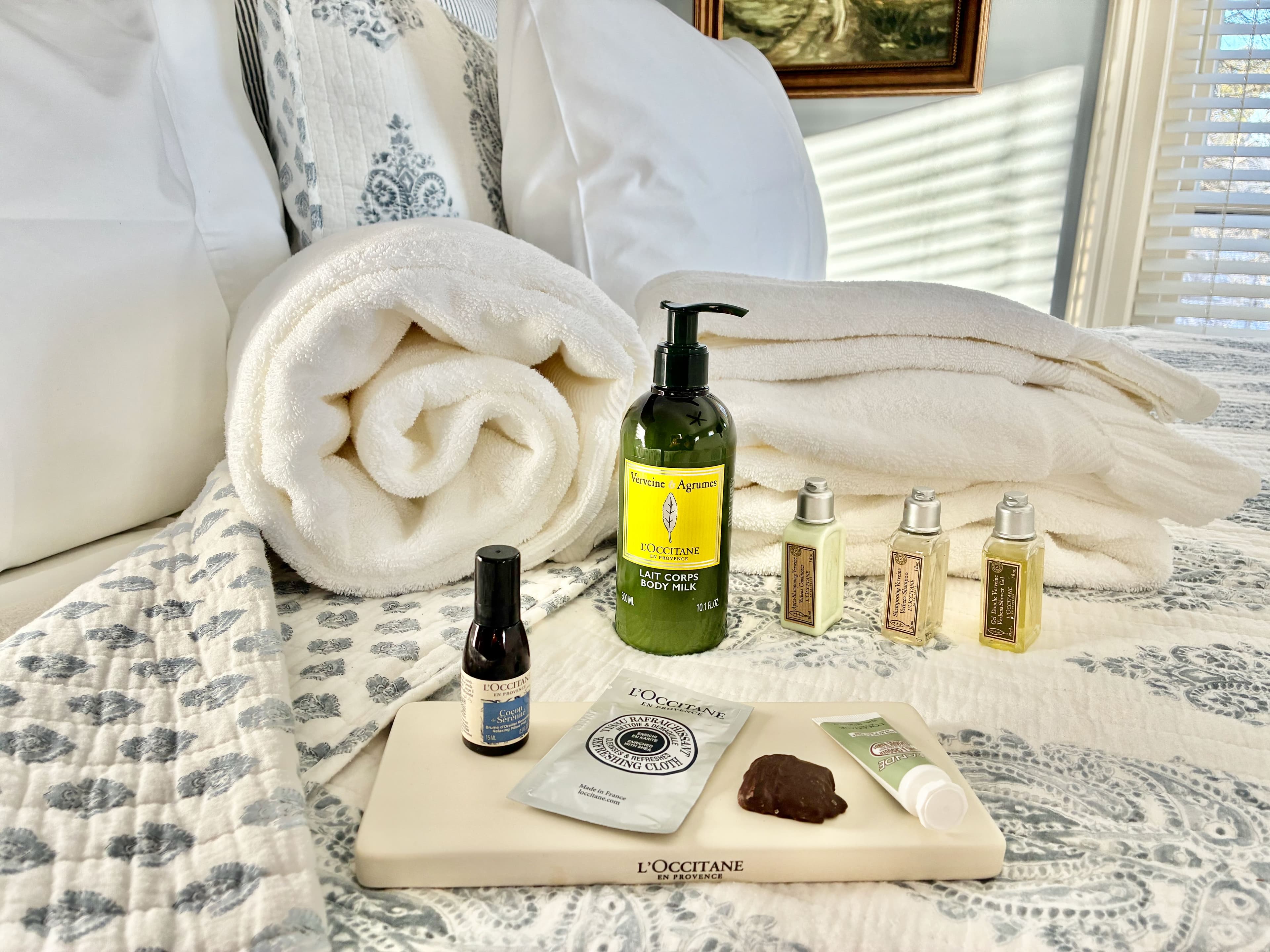 A neatly arranged spa setup featuring towels, L'Occitane body products, and a wooden tray.