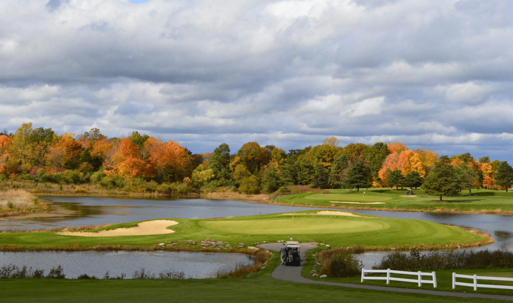 A scenic golf course surrounded by vibrant autumn foliage and a tranquil pond under a cloudy sky. A scenic golf course surrounded by vibrant autumn foliage and a tranquil pond under a cloudy sky.
