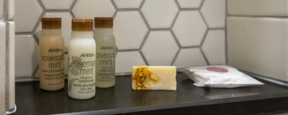 Avaida Rosemary Mint shampoo and conditioner bottles alongside a bar of soap and a wrapped item on a black shelf.