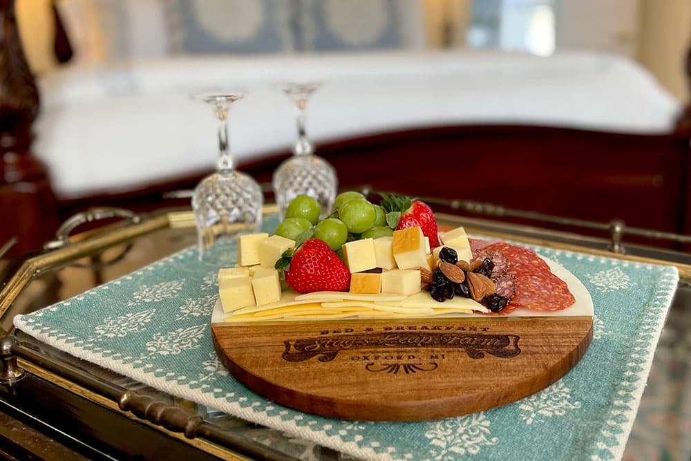 A gourmet cheese and charcuterie board featuring assorted cheeses, grapes, strawberries, salami, and nuts, accompanied by two crystal glasses on a decorative cloth.