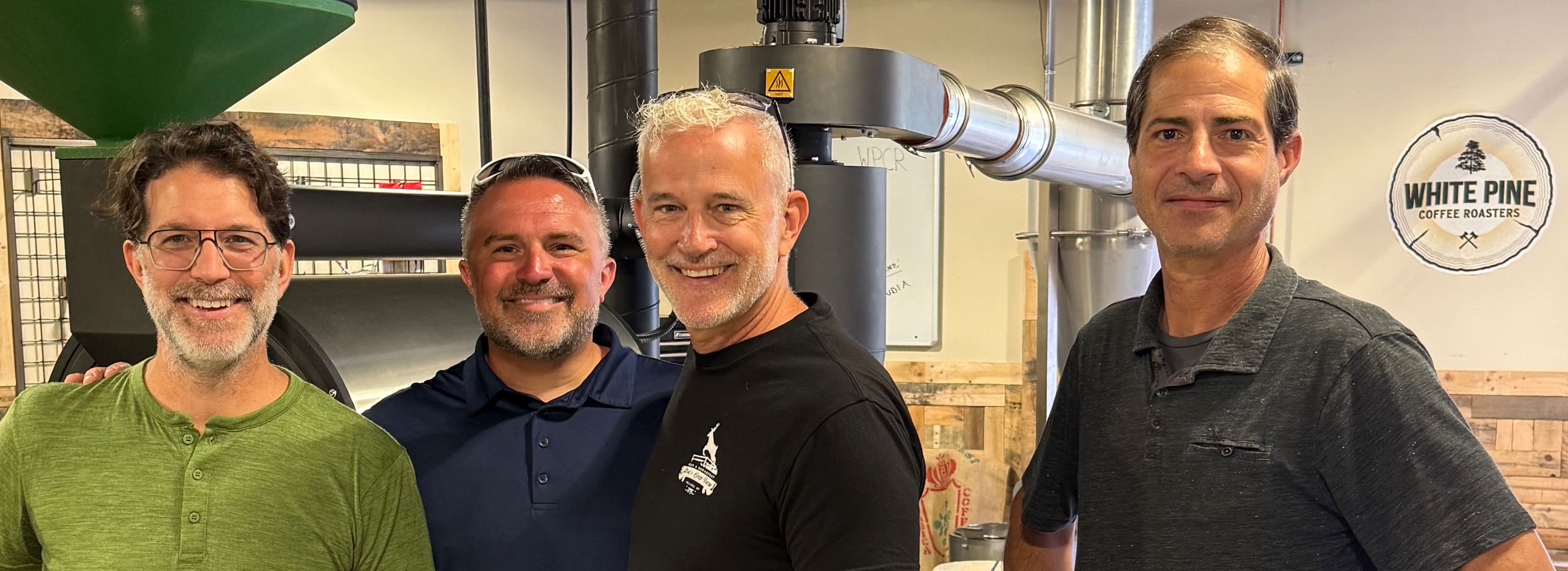 Four smiling men pose together in a coffee roasting facility.
