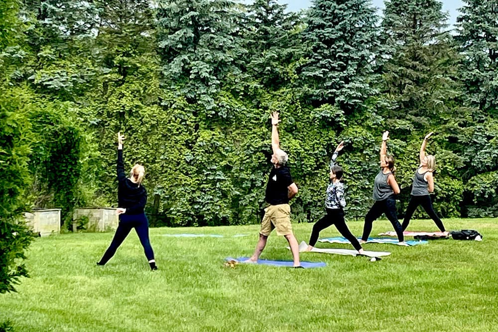A group of people practicing yoga outdoors on green grass.
