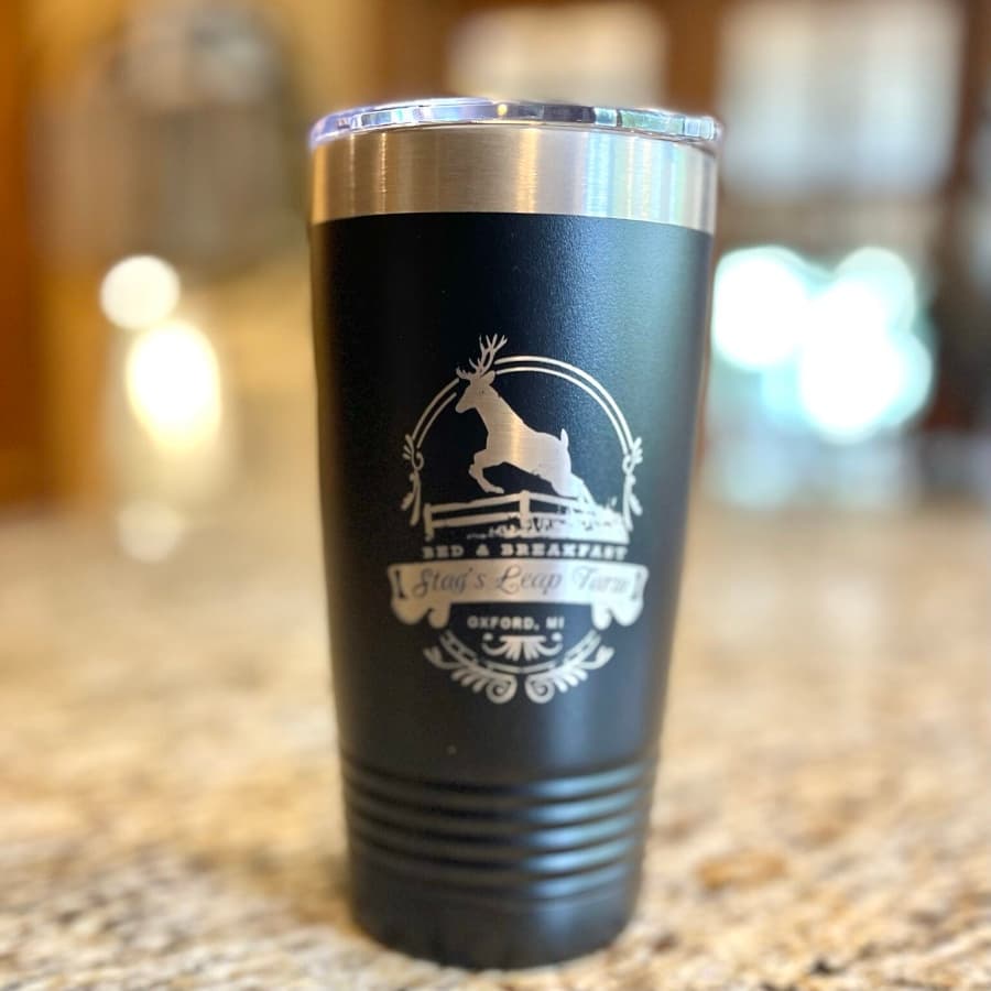 A black travel mug with a silver lid and a logo featuring a deer and the text "Stag's Leap Farm, Oxford, MI."