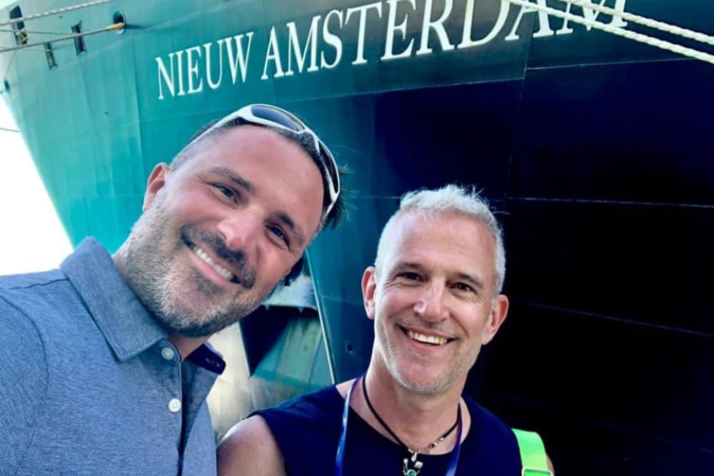Two smiling men take a selfie in front of the ship "Nieuw Amsterdam."