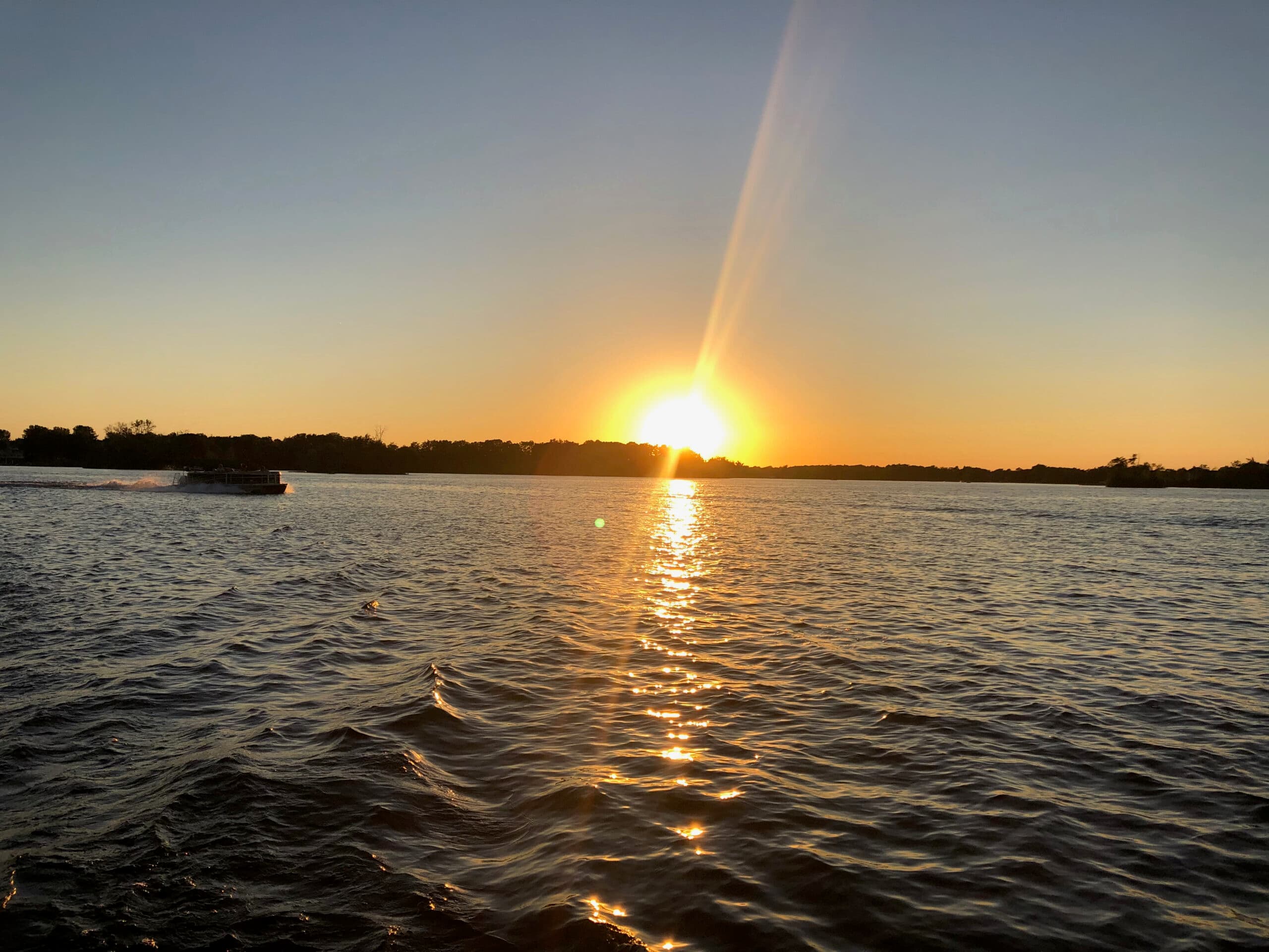 A vibrant sunset reflects on calm water with a boat in the distance.