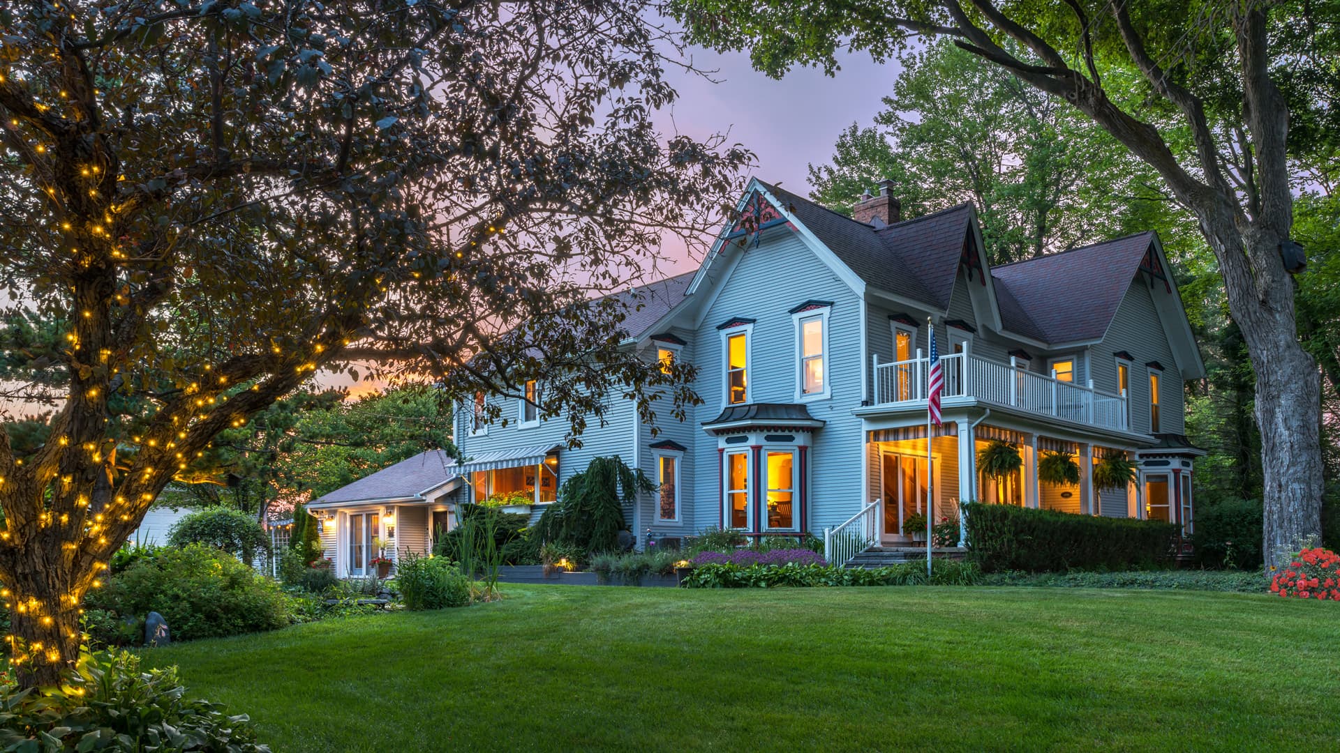 A beautiful Victorian-style house surrounded by lush greenery at sunset.