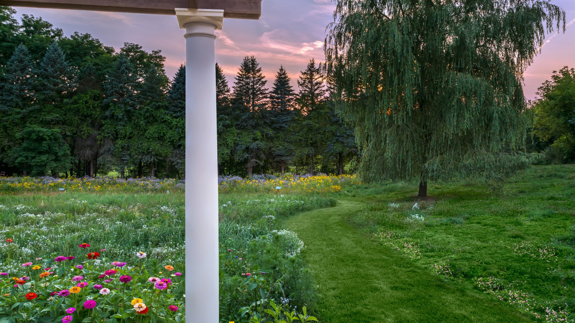 A vibrant garden with colorful flowers leading to a grassy path under a sunset sky.